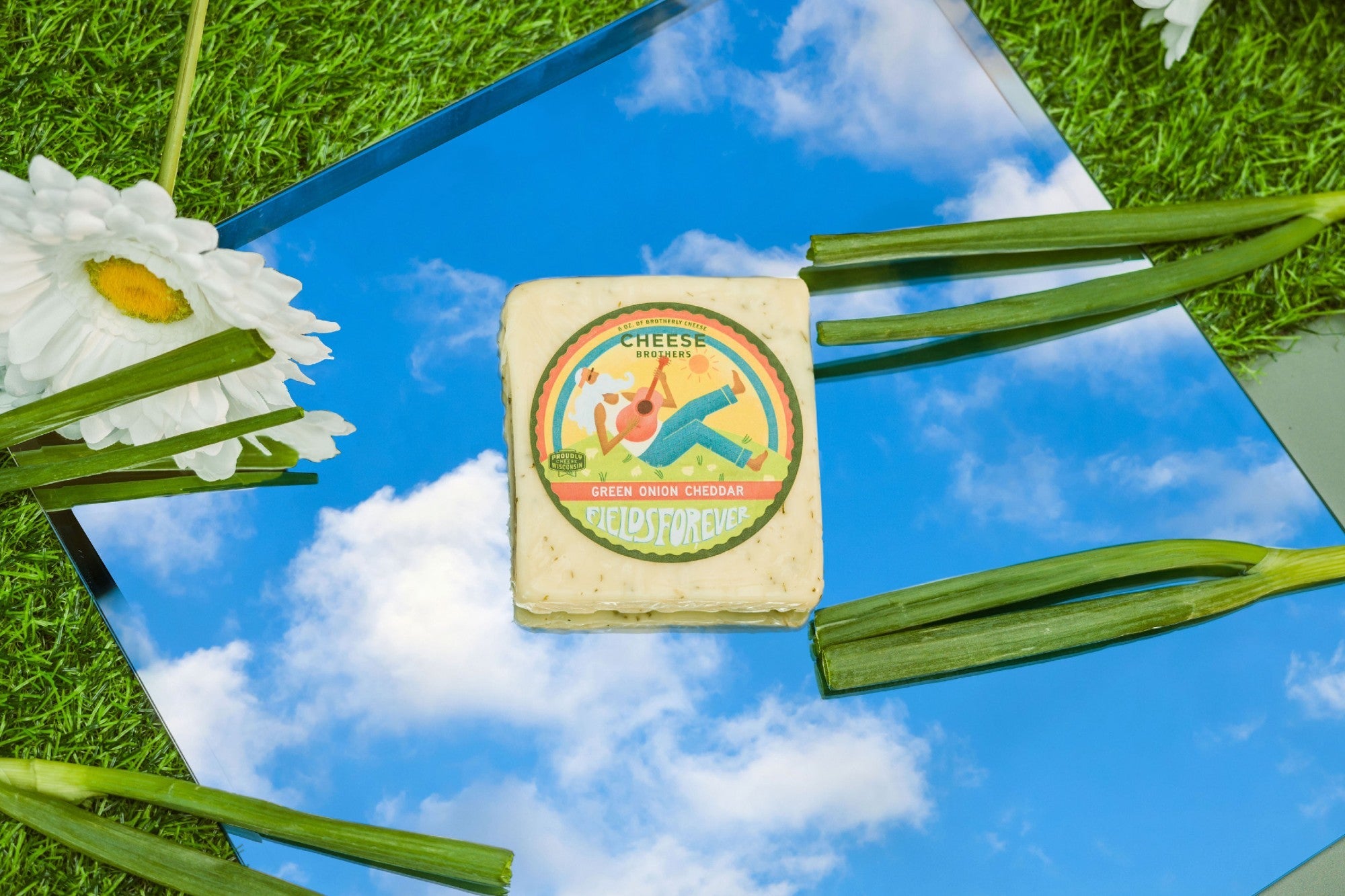Creamy green onion cheddar cheese from Cheese Brothers, Inc., featuring fresh green onion pieces in a smooth cheddar block.