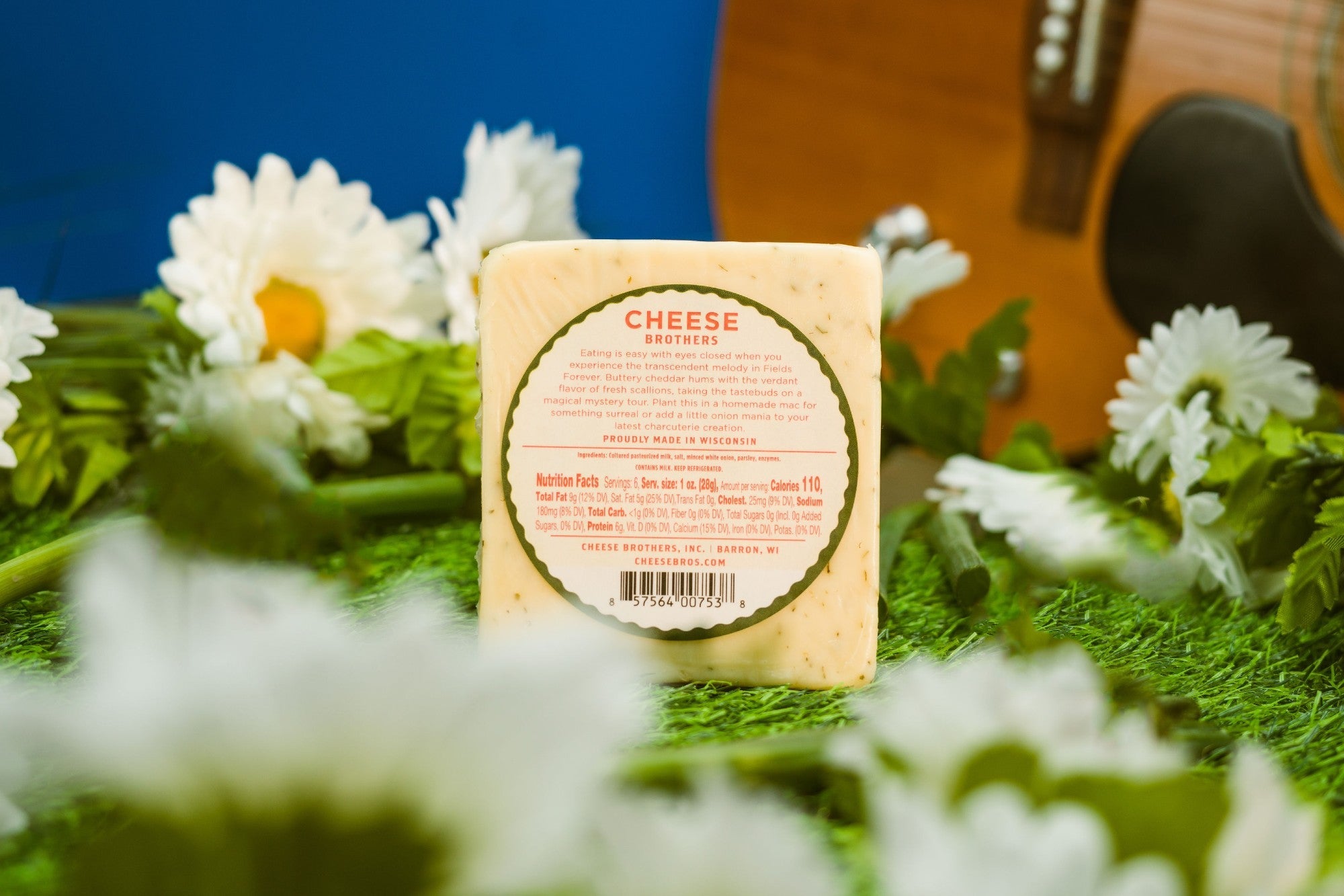 Creamy cheddar cheese block with green onion pieces from Cheese Brothers, Inc., set against a rustic field background.