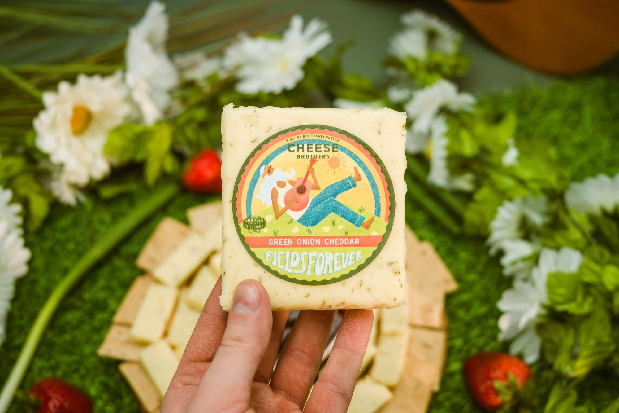 Creamy green onion cheddar cheese from Cheese Brothers, Inc., showcasing a block of cheese with fresh green onion bits.