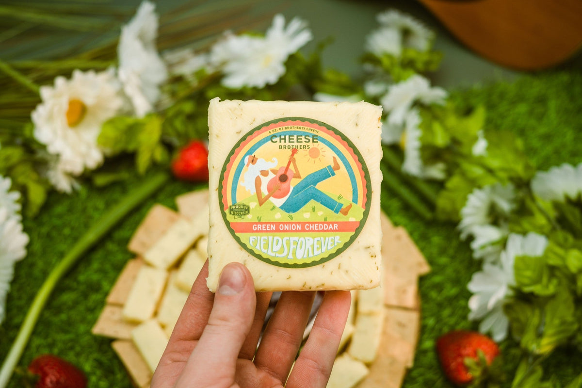 Creamy green onion cheddar cheese from Cheese Brothers, Inc., showcasing a block of cheese with fresh green onion bits.