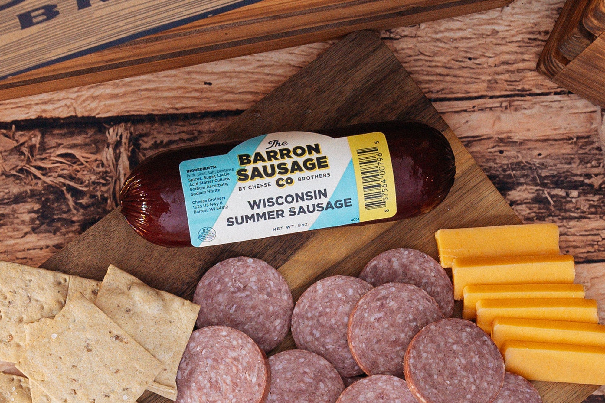 Slices of Barron Sausage Co. Summer Sausage, a cured meat, displayed on a wooden board with cheese and crackers.