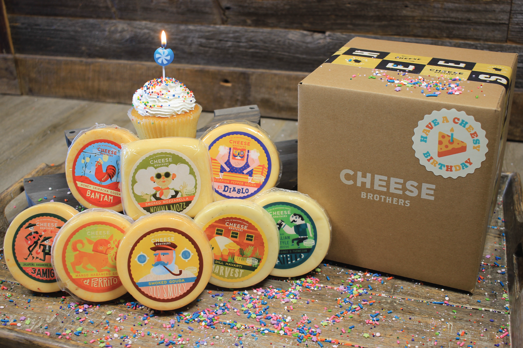 Cheesy birthday gift basket from Cheese Brothers, Inc. with assorted cheeses, snacks, and birthday-themed treats in a colorful box.
