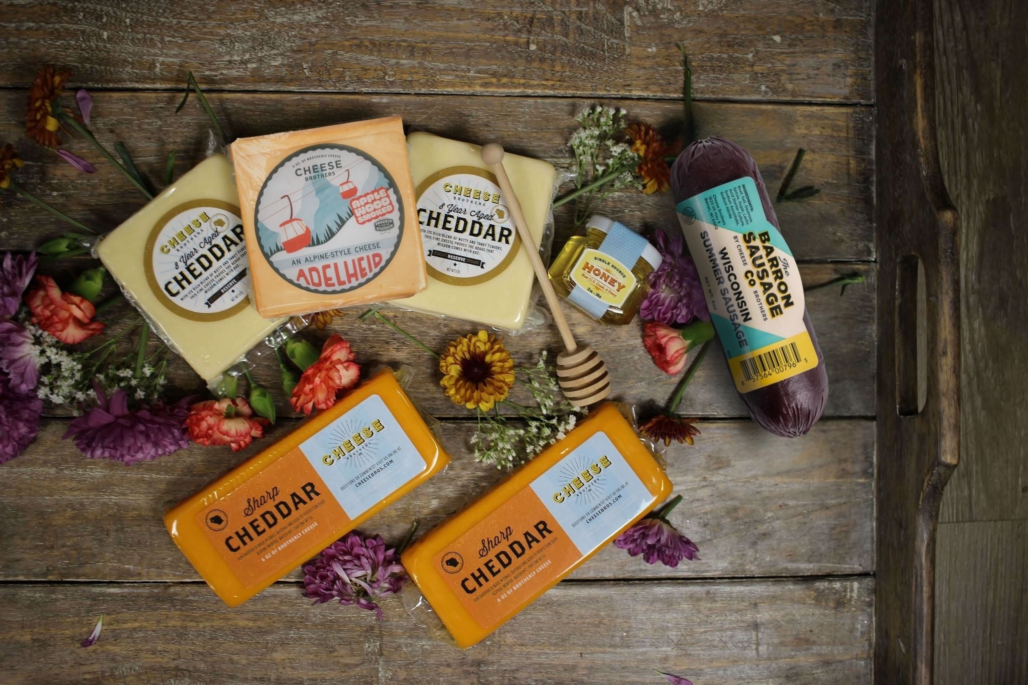 Cheese Brothers, Inc. "Hope You're Feeling Cheddar Soon" gift basket with assorted cheeses and snacks in a decorative basket.