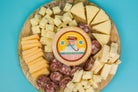 Assorted cheese and meat charcuterie pack from Cheese Brothers, Inc., arranged with crackers and fresh fruits on a wooden board.