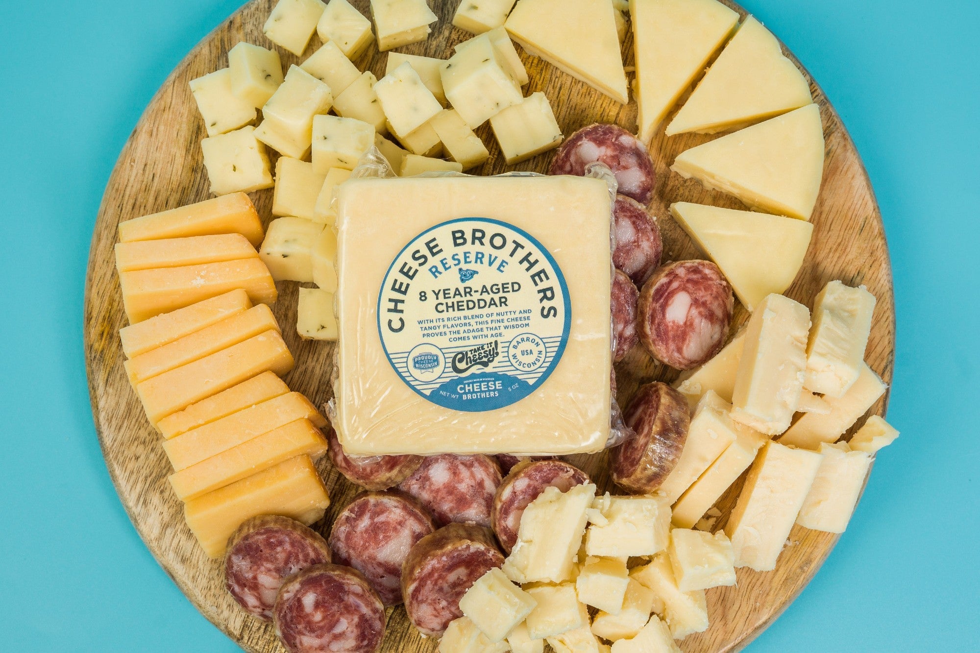 Assorted cheese and cured meat charcuterie platter from Cheese Brothers, Inc. with crackers and garnishes on a wooden board.