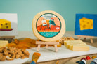Slice of classic Gouda cheese from Cheese Brothers, Inc., showing its smooth, pale yellow surface on a wooden board.