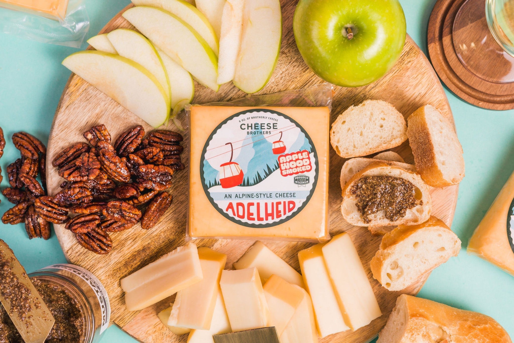 Adelheid Alpine-Style Cheese from Cheese Brothers, Inc. with a wine pairing, showcasing a creamy cheese wheel on a rustic wooden board.
