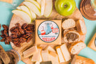 Adelheid Alpine-Style Cheese from Cheese Brothers, Inc. with a wine pairing, showcasing a creamy cheese wheel on a rustic wooden board.