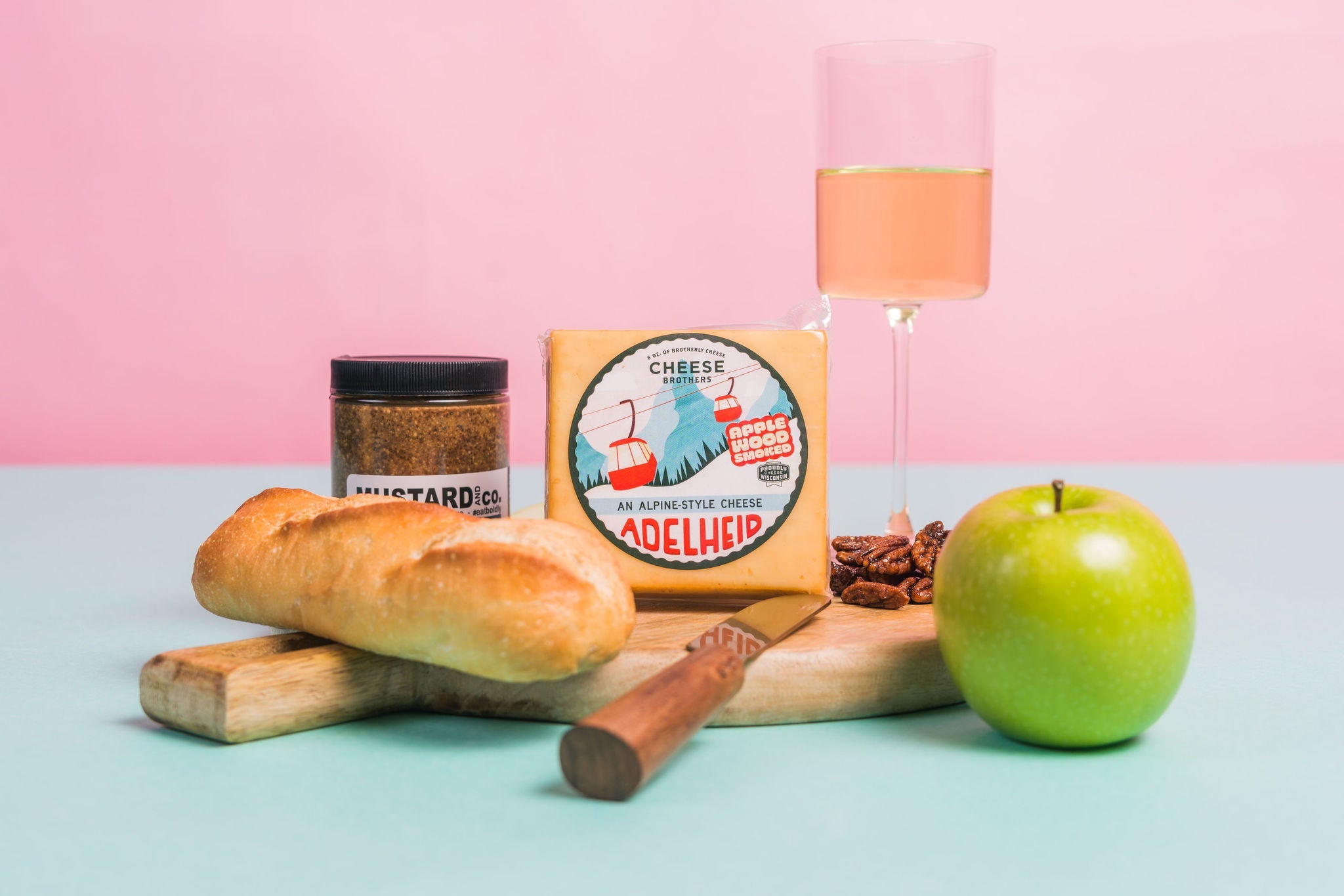 Creamy Adelheid Alpine-style cheese from Cheese Brothers, Inc., displayed on a wooden platter with wine and bread.