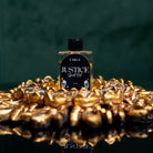 Justice Ritual Oil by Circe Boutique in a glass bottle, with a label and surrounding ritual herbs on a dark surface.