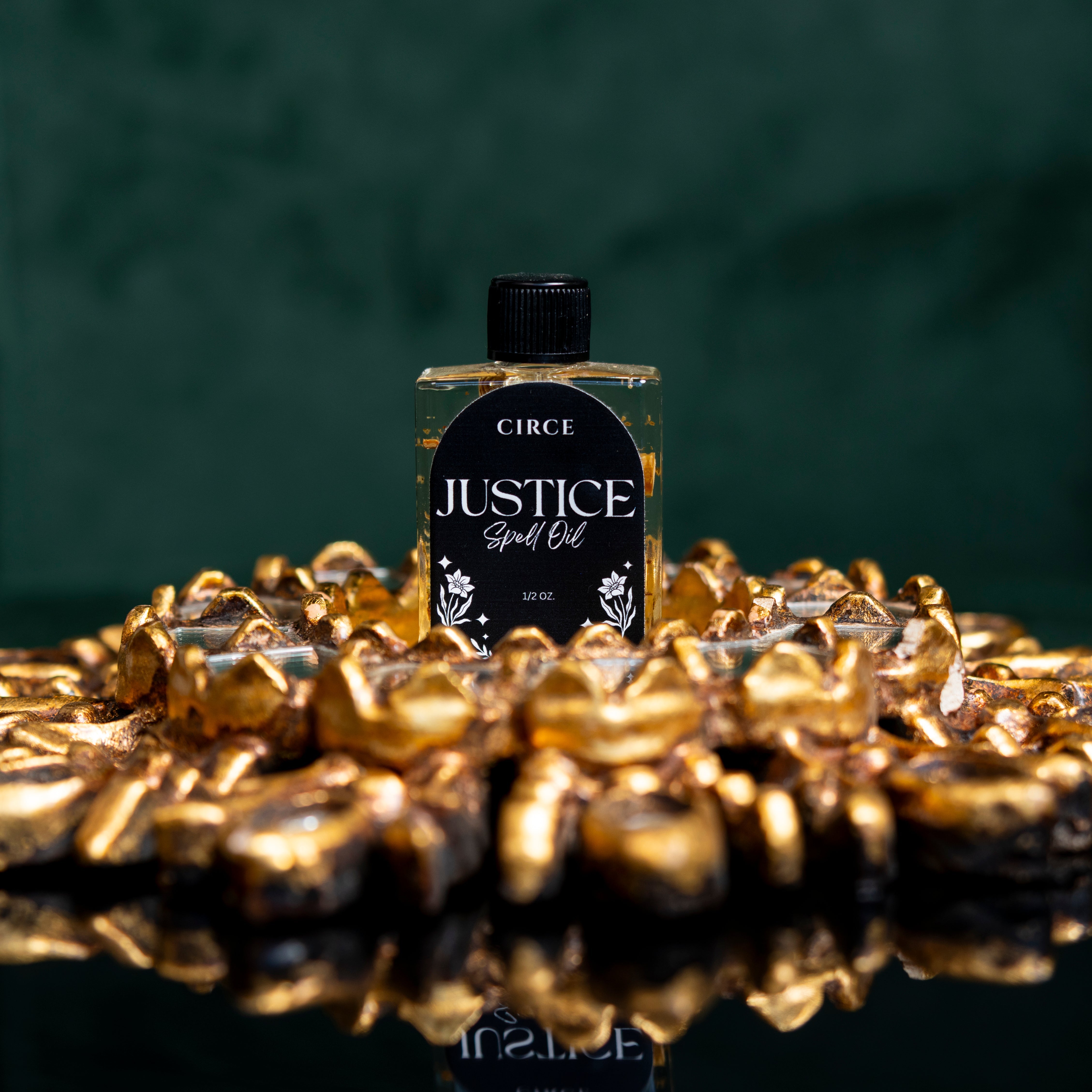 Justice Ritual Oil by Circe Boutique in a glass bottle, with a label and surrounding ritual herbs on a dark surface.