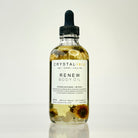 Crystal Irie ReNew Body Oil bottle with golden liquid and label, lying on a soft surface, showcasing the nourishing body oil product.