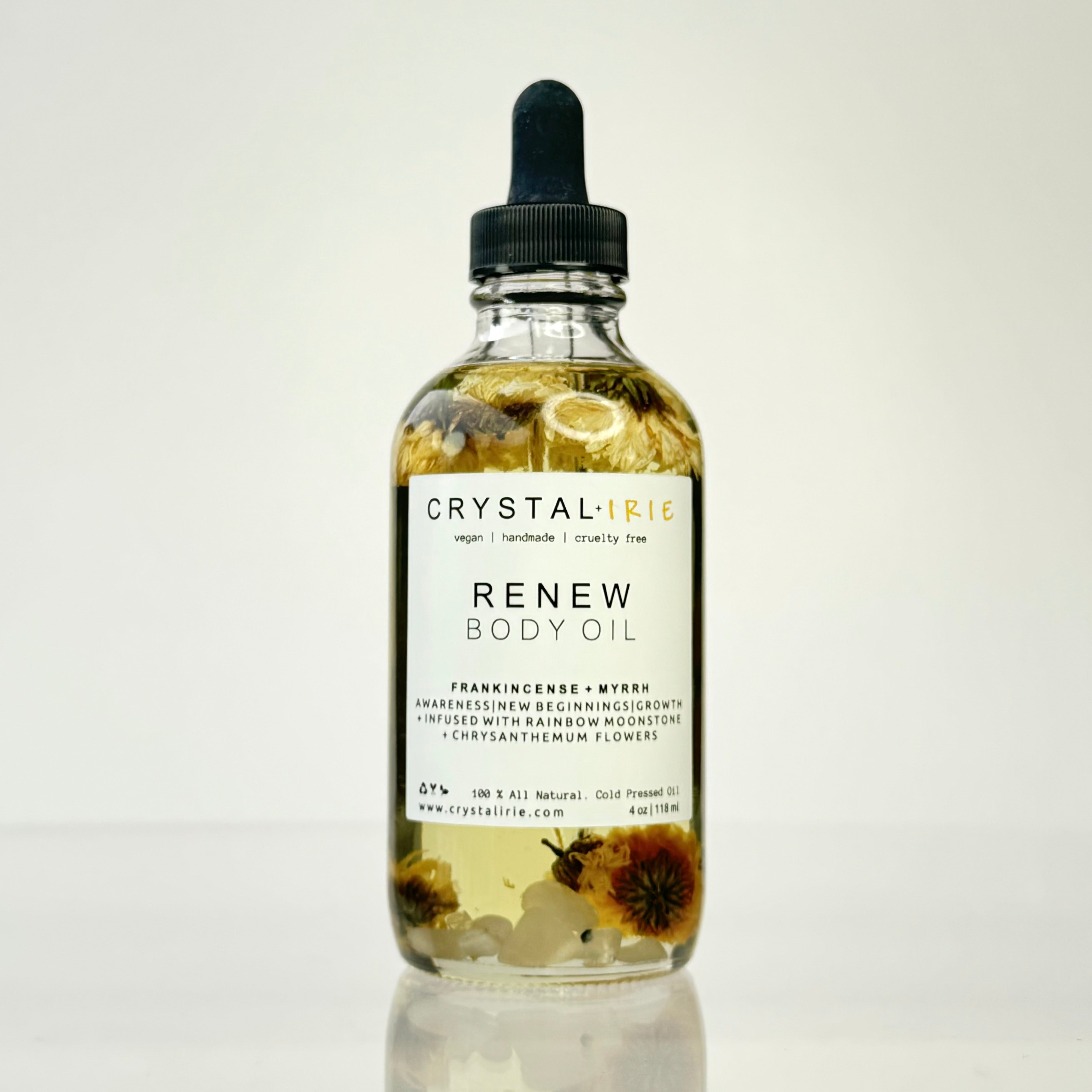 Crystal Irie ReNew Body Oil bottle with golden liquid and label, lying on a soft surface, showcasing the nourishing body oil product.