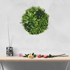 Artificial green wall disc with white frame from Designer Plants USA, UV resistant living wall with potted plants for commercial use.