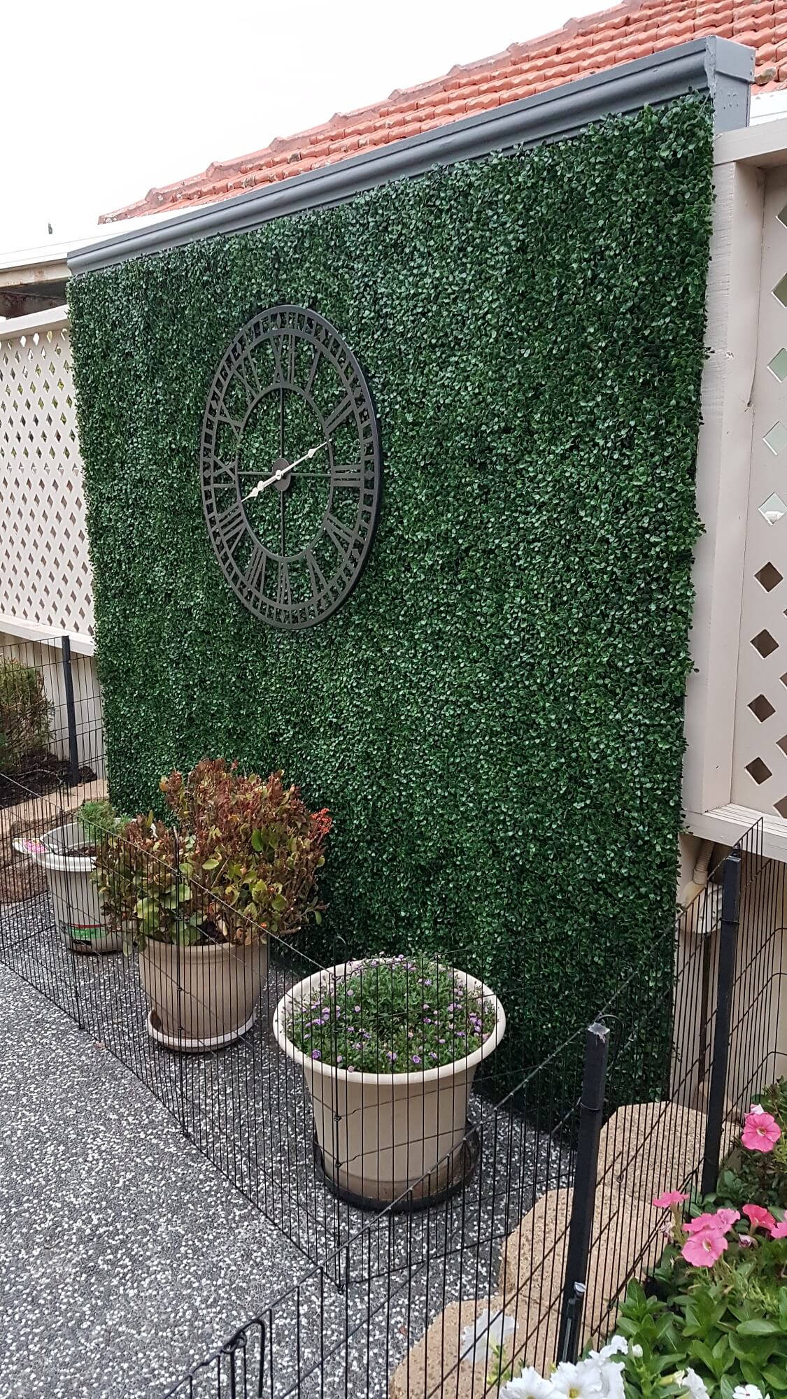 Dark green boxwood artificial vertical garden panels from Designer Plants USA installed as a living wall with decorative clock art.