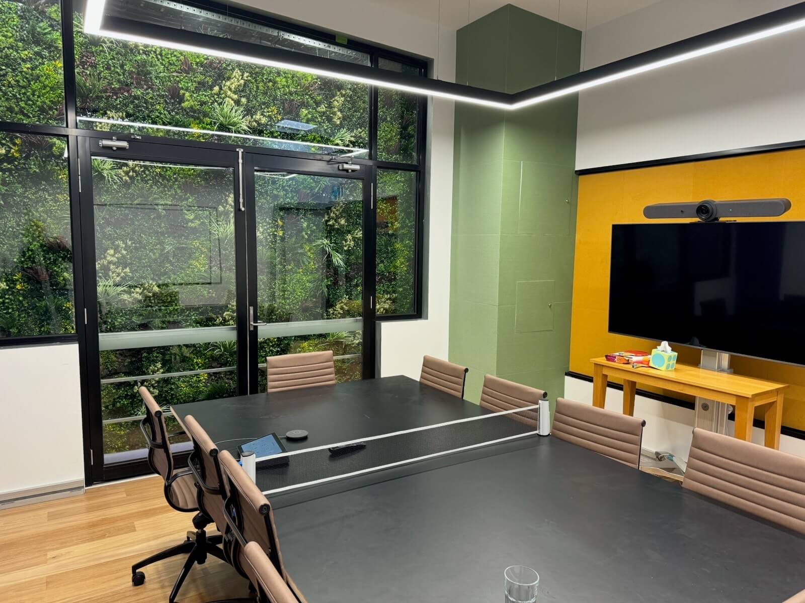 Office boardroom with Designer Plants USA evergreen triptych artificial green wall panels, creating a lush, UV-resistant living wall.