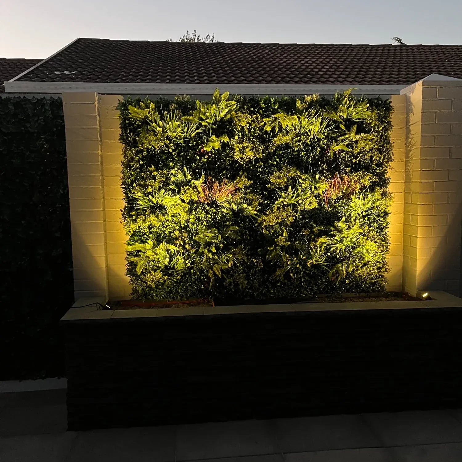 Lush Spring artificial vertical garden panel by Designer Plants USA, UV resistant living wall with vibrant green foliage at night.