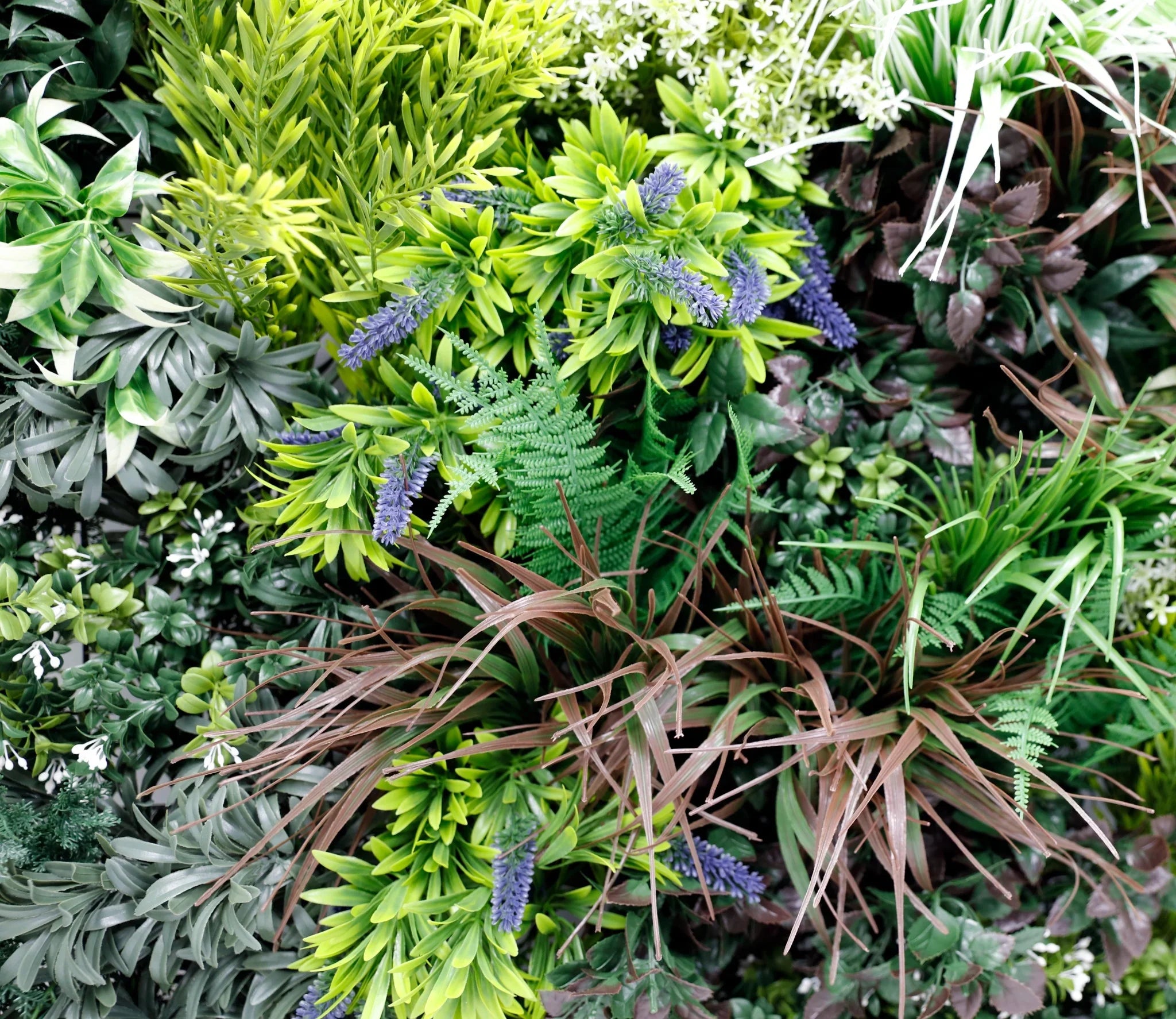 Close-up of lush tropical forest-inspired artificial green wall panel with mixed greenery, UV resistant, fire-rated, Designer Plants USA.