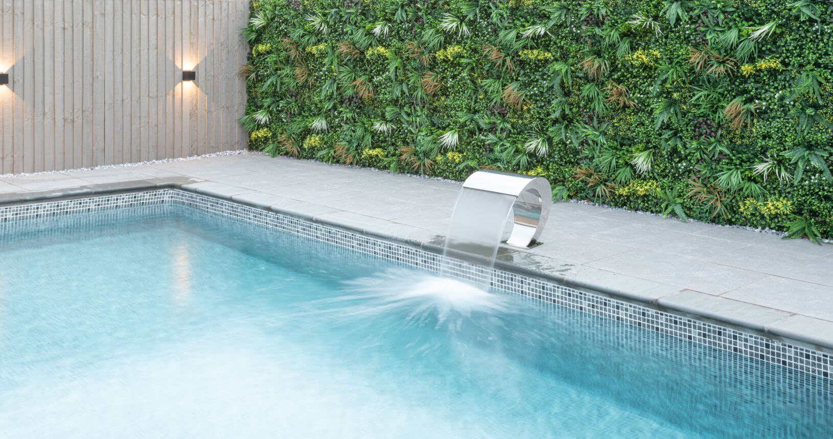 Wild Tropics artificial living wall panel by Designer Plants USA installed along pool fence with waterfall, UV resistant green wall.
