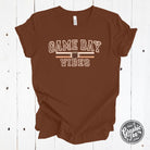 Graphic SS football T-shirt from The Graphic Tee with "Game Day Vibes" design, featuring football graphics and vibrant colors.