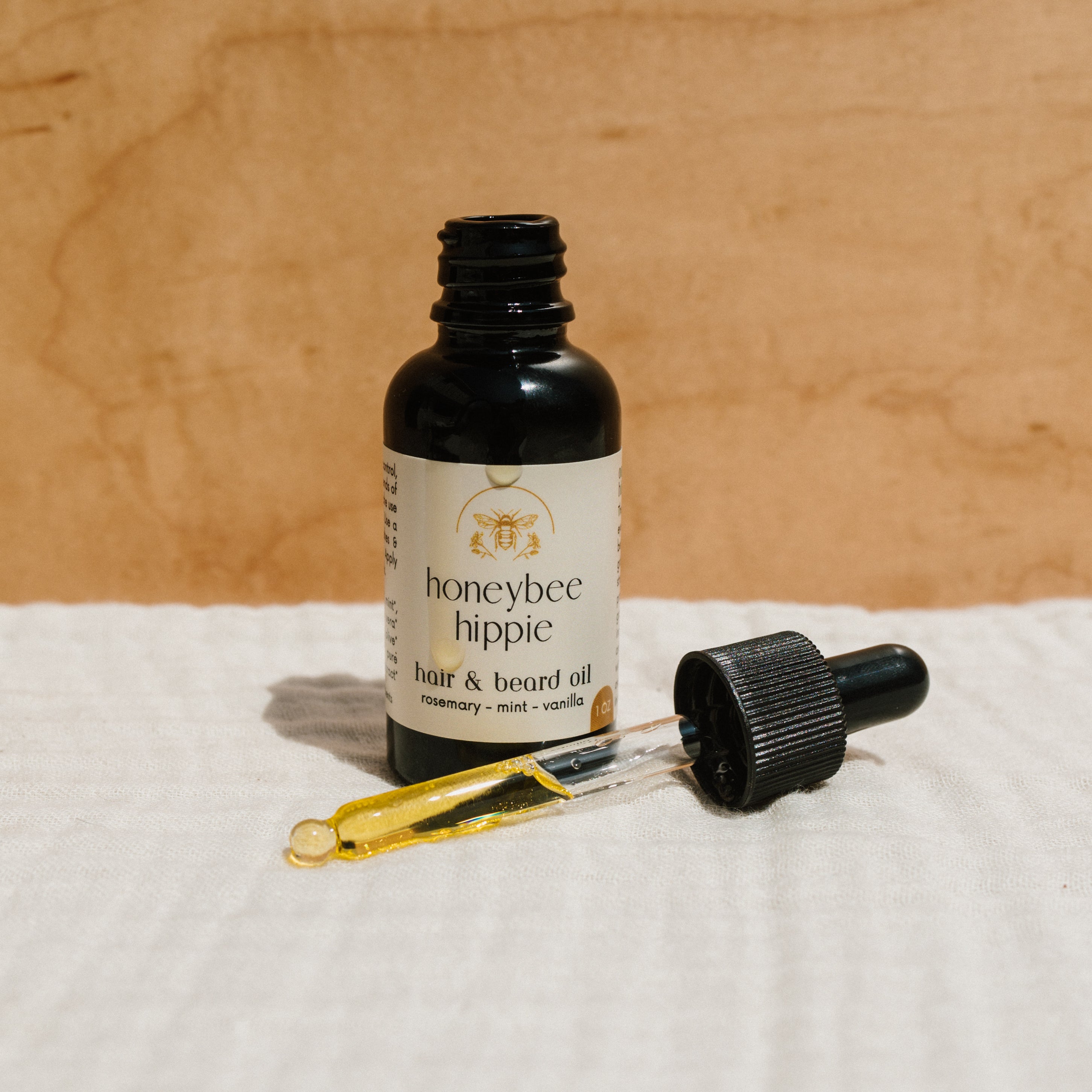 Bottle of Honeybee Hippie hair and beard oil with natural ingredients, showcasing the product label and dropper applicator.