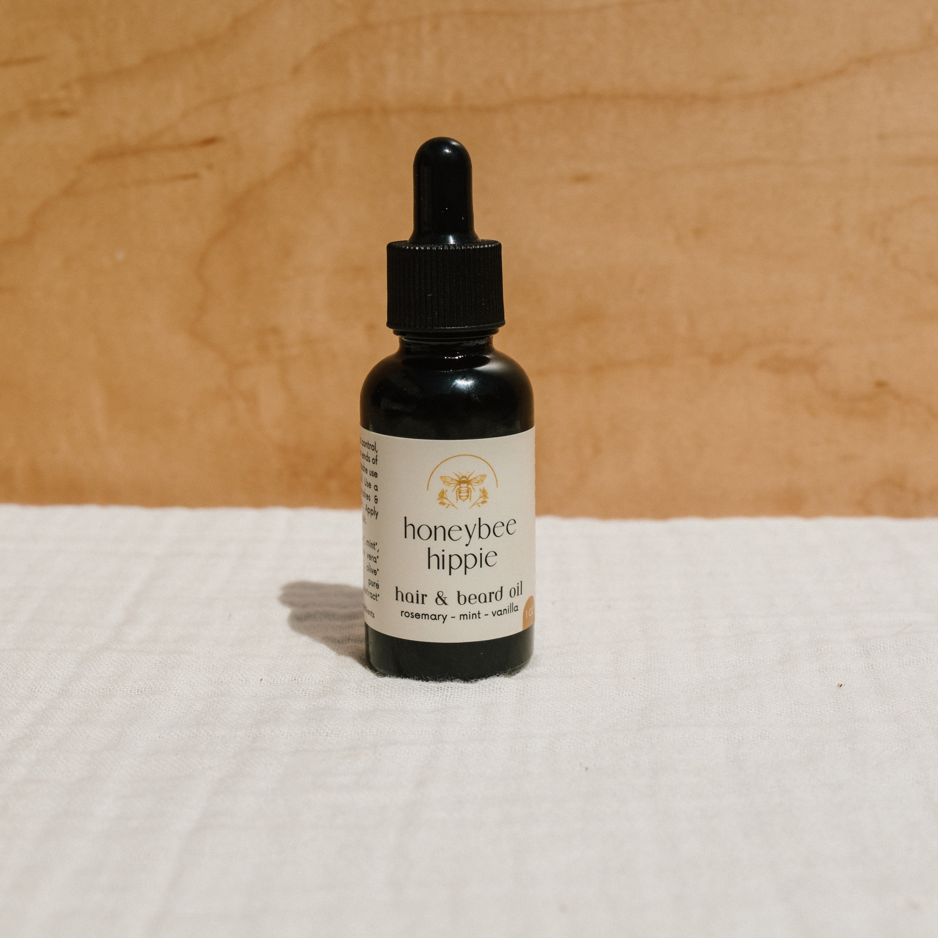 Bottle of Honeybee Hippie hair and beard oil with natural ingredients, showcasing a sleek, amber-colored glass container.