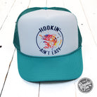 Foam trucker cap with "Hookin' Ain't Easy" graphic from The Graphic Tee, featuring a mesh back and adjustable strap.