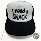 Foam trucker cap with "I Need A Snack" graphic by The Graphic Tee, featuring a structured brim and adjustable snapback closure.