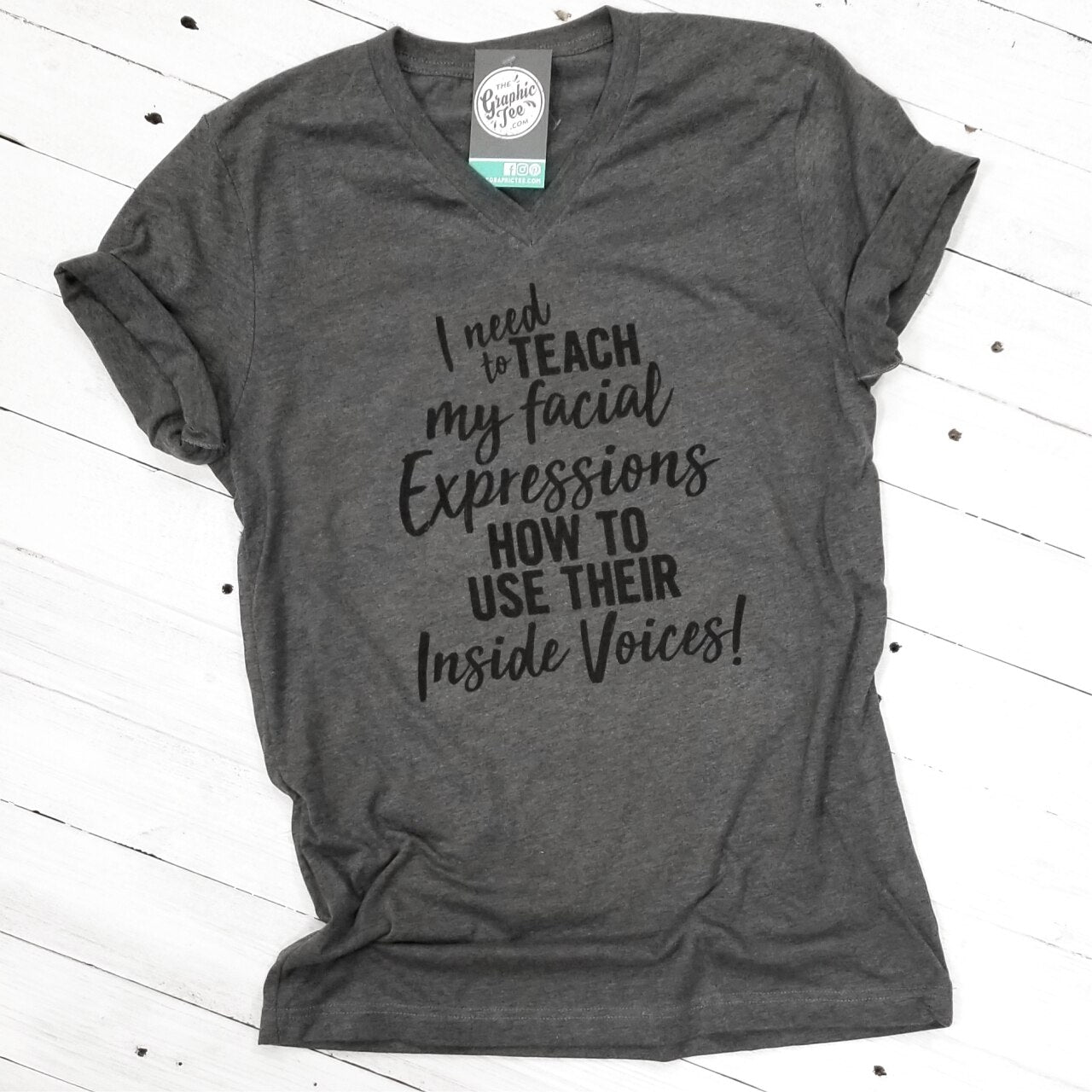 White V-neck T-shirt from The Graphic Tee featuring humorous "I Need to Teach My Facial Expressions" graphic design.
