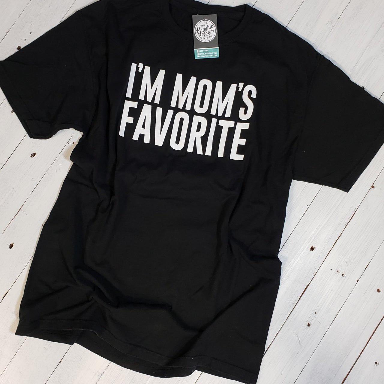 Black short-sleeve graphic tee by The Graphic Tee with "I'm Mom's Favorite" printed design.