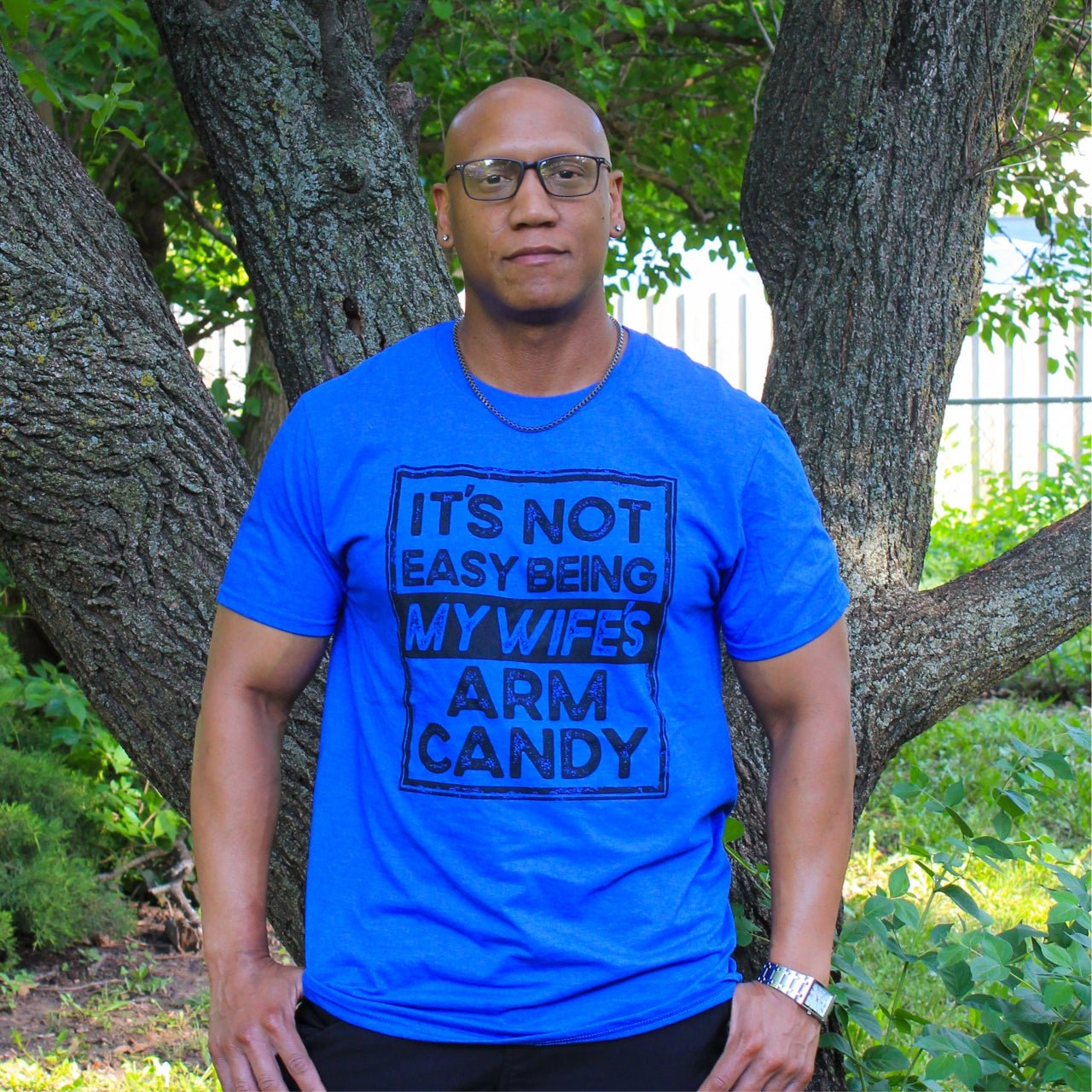 Adult SS graphic tee from The Graphic Tee with humorous "It's Not Easy Being My Wife's Arm Candy" design.