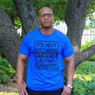 Adult SS graphic tee from The Graphic Tee with humorous "It's Not Easy Being My Wife's Arm Candy" design.
