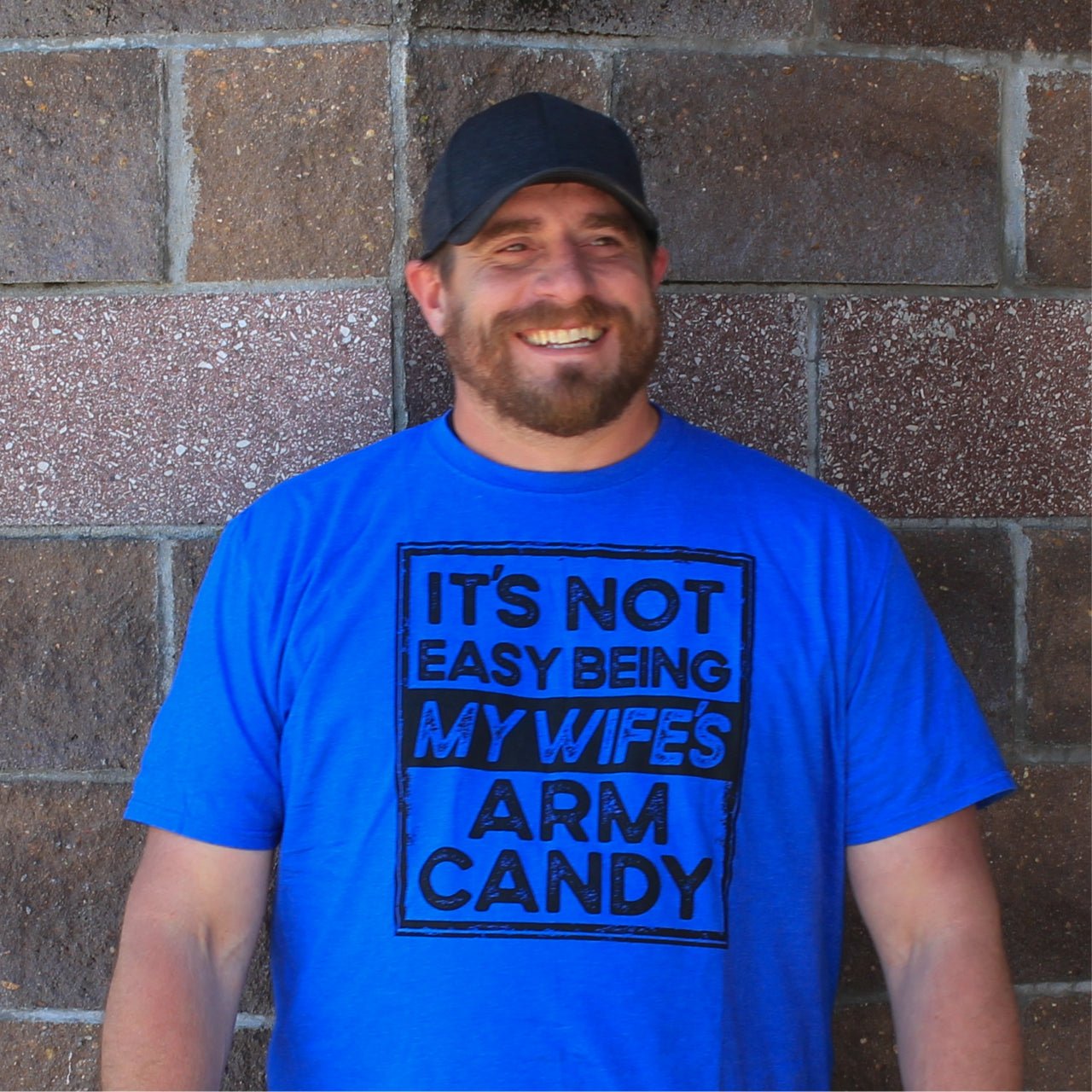Adult short sleeve graphic tee from The Graphic Tee featuring humorous "It's Not Easy Being My Wife's Arm Candy" design.