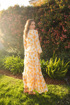 Elegant yellow Jennafer Grace Love Maxi Dress displayed on a hanger with flowing fabric and floral accents, perfect for summer wear.