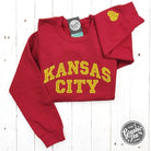 Dark red crewneck sweatshirt by The Graphic Tee featuring Kansas City gold glitter applique design.