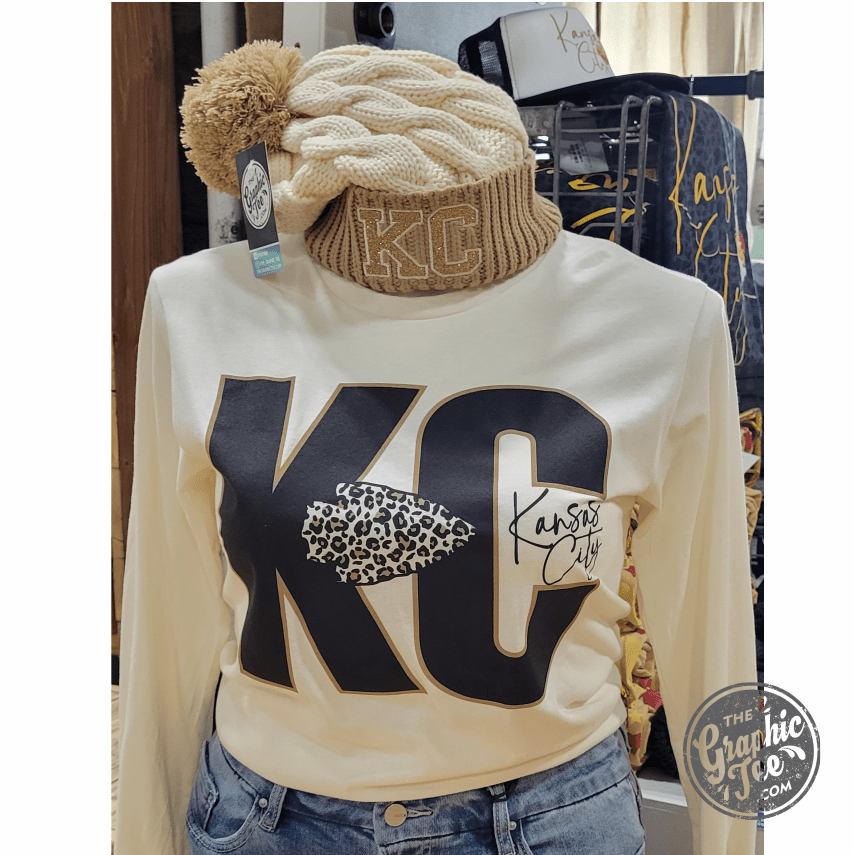Black KC Glitter Applique Twist Knit Beanie with Pom by The Graphic Tee, featuring a glittery logo and cozy knit design.