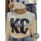 Black KC Glitter Applique Twist Knit Beanie with Pom by The Graphic Tee, featuring a glittery logo and cozy knit design.