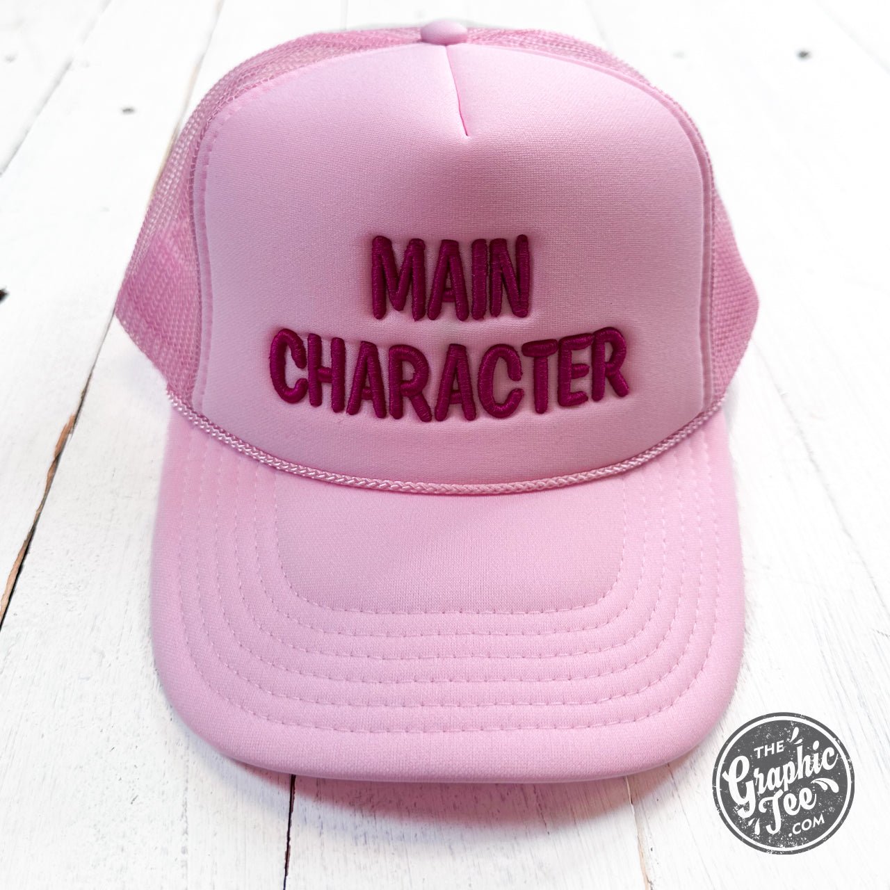 Embroidered trucker cap featuring main character design by The Graphic Tee, with mesh back and adjustable strap.