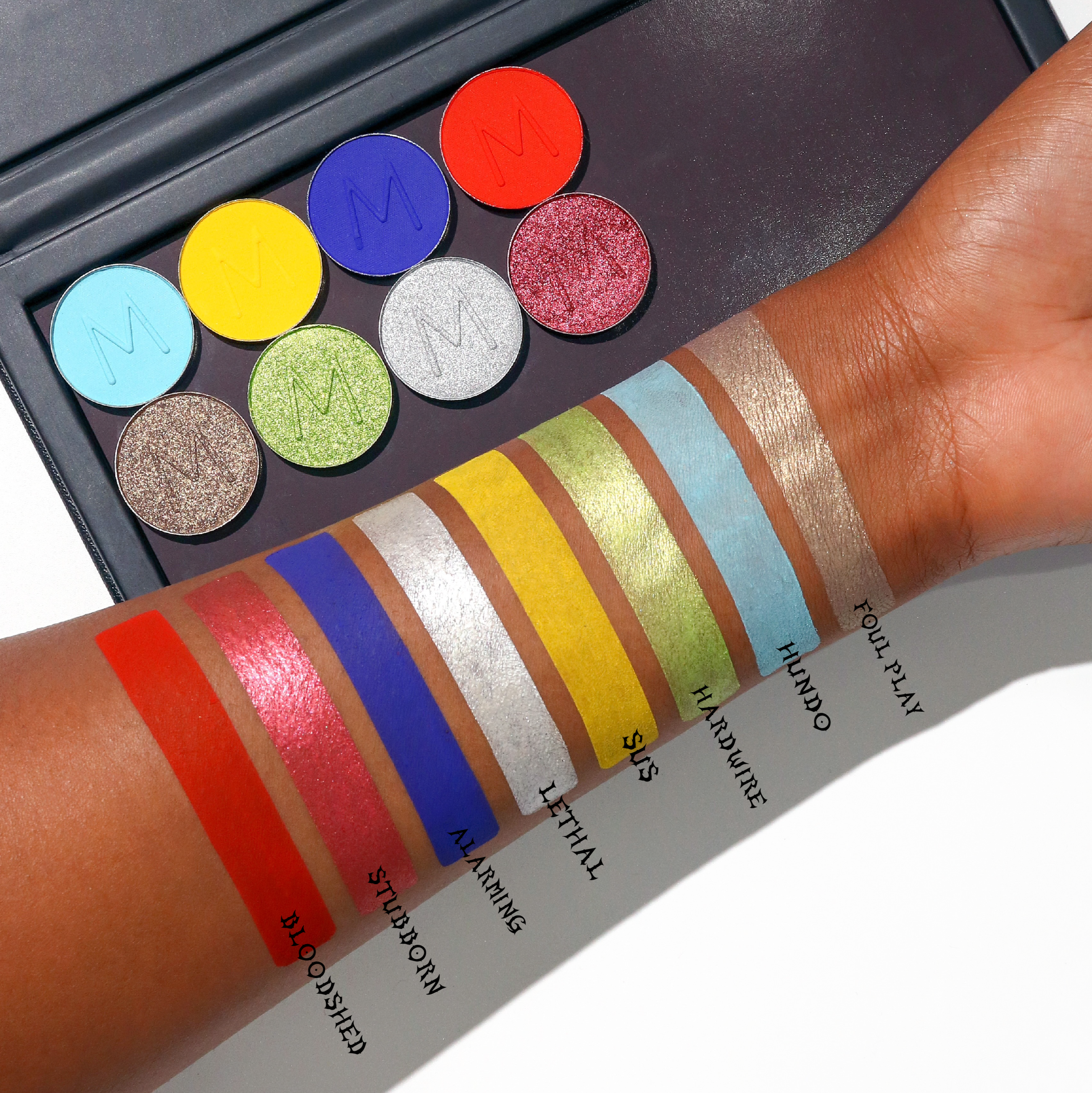 Eyeshadow lineup by Makeup A Murder, INC featuring various shades of eye shadow in a colorful palette display.