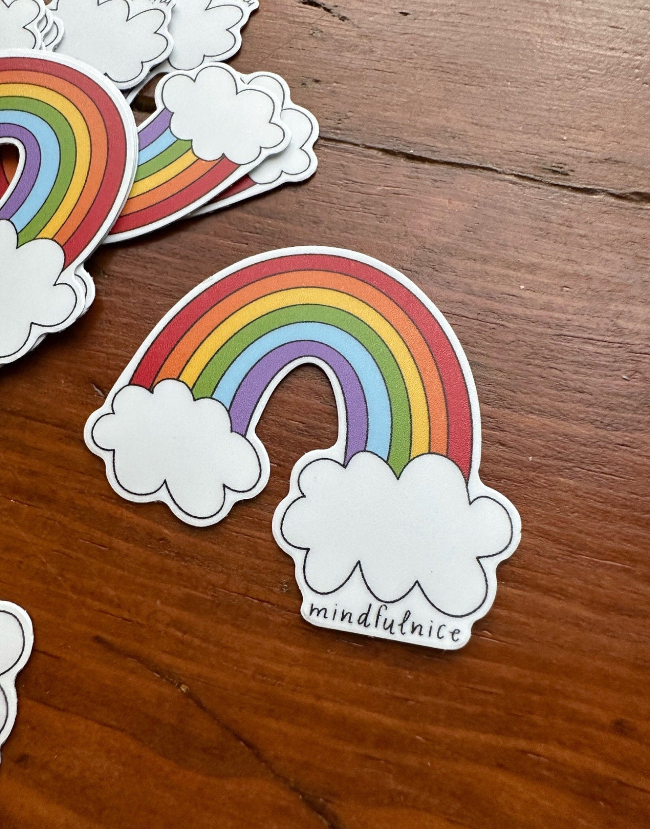 Colorful rainbow sticker by Mindfulnice featuring vibrant, eye-catching design on a clear backing for decorating notebooks or laptops.