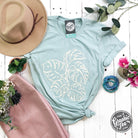 The Graphic Tee Monstera Crewneck Short Sleeve Tee with a green monstera leaf graphic on a casual short sleeve shirt.