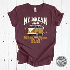 Heather maroon short sleeve graphic tee featuring "My Dream Job...Driving The Karma Bus" text from The Graphic Tee brand.