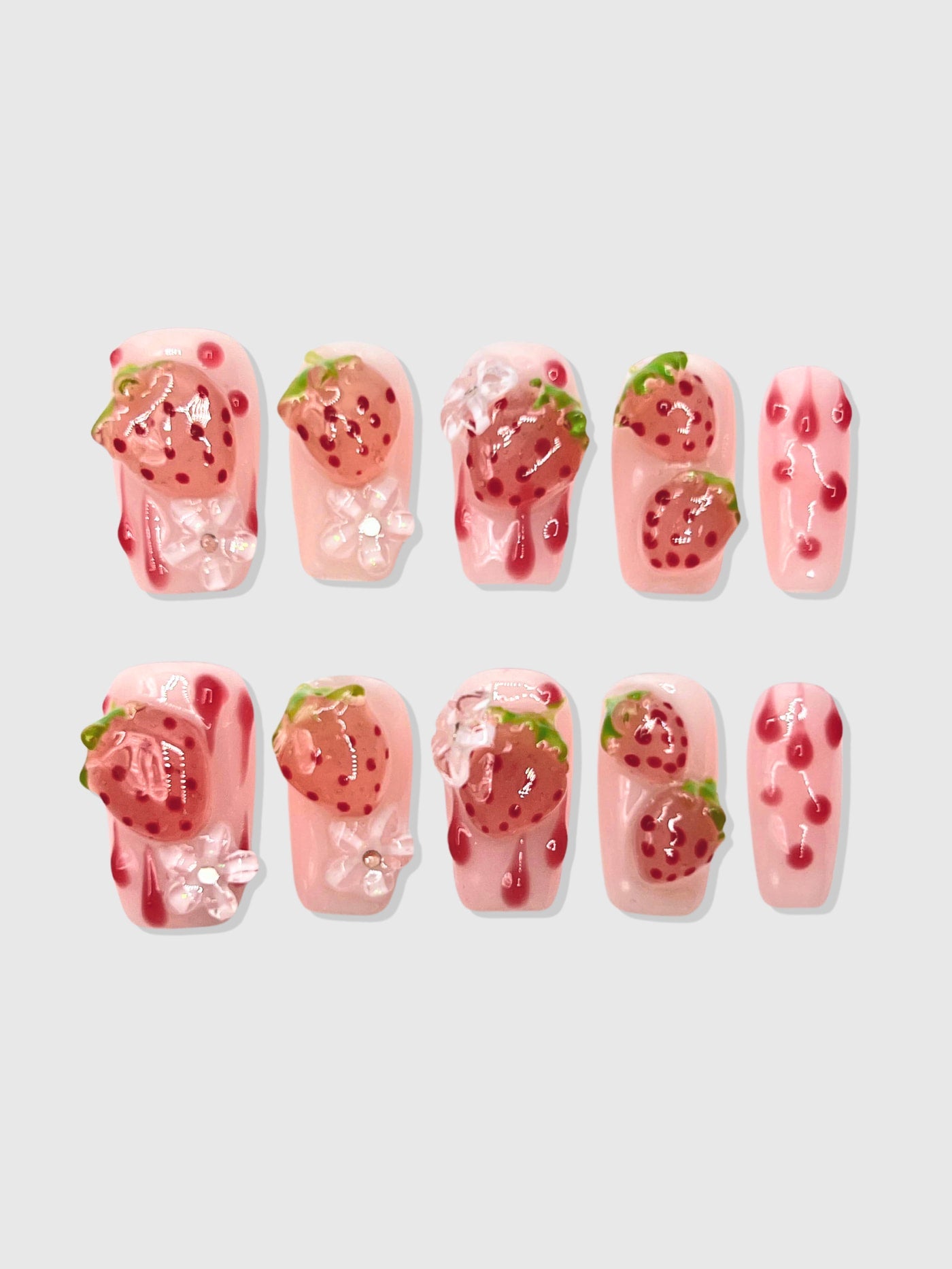 Nekoyanin strawberry shortcake press-on nails with pink and red strawberry designs on a clear base, showcasing a cute, decorative manicure.