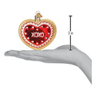 Red heart-shaped cookie ornament with white decorative details from Old World Christmas, hanging with a silver string.