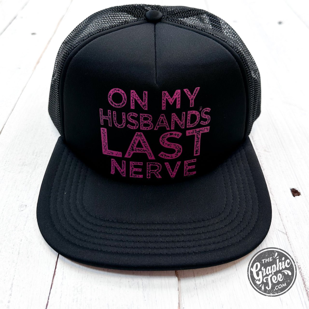 Black foam trucker cap with bold "On My Husband's Last Nerve" graphic, casual accessory by The Graphic Tee.