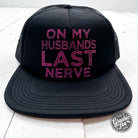 Black foam trucker cap with "On My Husband's Last Nerve" slogan, featuring a curved brim and adjustable snapback closure.