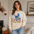 Colorful watercolor haunted house Halloween sweatshirt with ghost and pumpkin design by OrnamentallyYou, featuring vibrant spooky artwork.