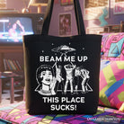Black canvas tote bag featuring a retro UFO meme and sarcastic "Beam Me Up This Place Sucks" text, stylish and humorous.