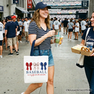 White tote bag featuring baseball-themed design with a coquette bow, perfect for game day or casual shopping.