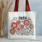 White canvas tote bag with "It's Okay" floral affirmation design by OrnamentallyYou, ideal for inspiring and kind women.